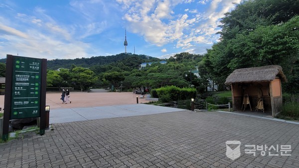 남산의 계곡물이 청학지로 흘러가는 다리와 오른쪽의 초가 건물내에 지게와 서울타워