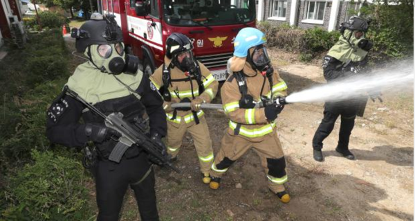 지난 24일 전개된 군·경·소방 합동 대테러훈련에서 신북119안전센터 소방관들이 모의 화재지점을 향해 물대포를 쏘는 가운데 육군2군단 군사경찰 특수임무대 장병들이 경계 임무를 수행하고 있다.(사진=육군제공)